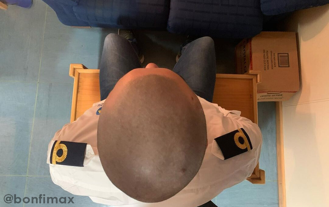 The bald head of a seafarer sitting down.