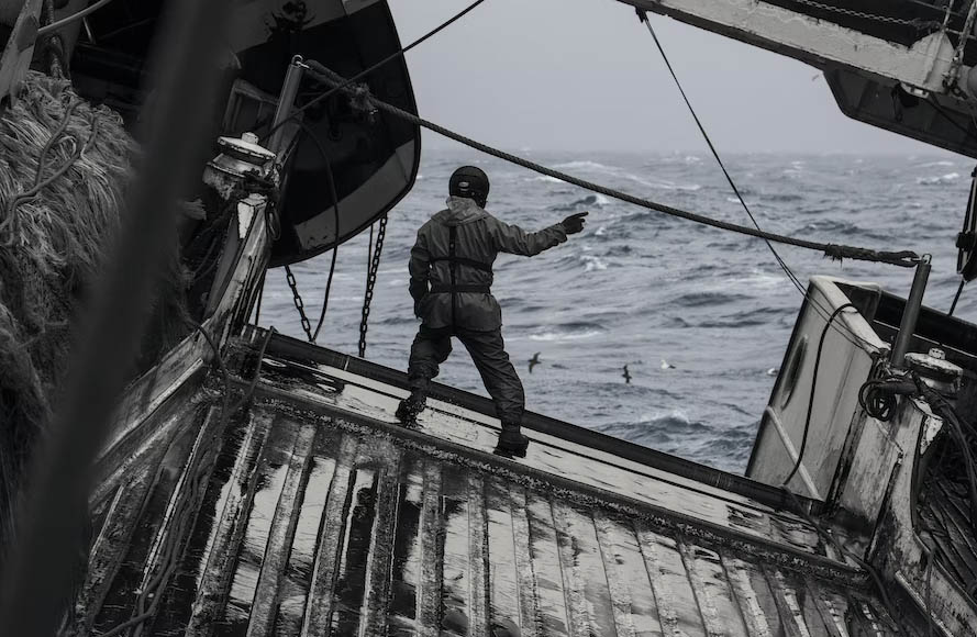 A seaman standing on deck and holding on to his balance as the ship rolls heavily while navigating.