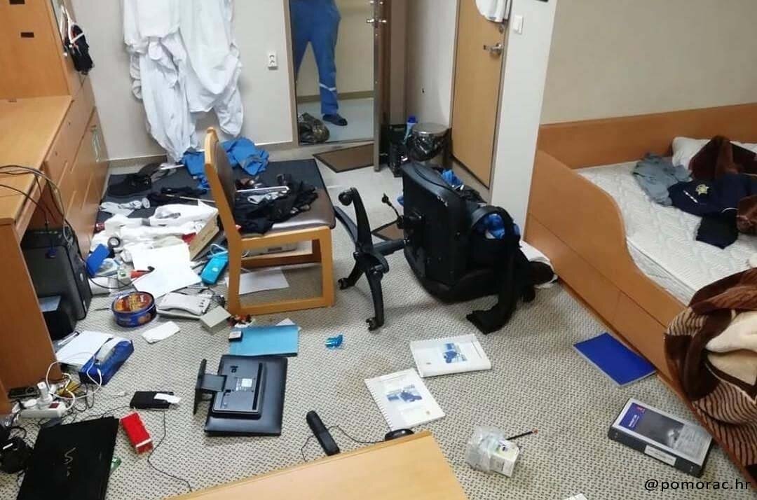 A seaman's cabin with all his things including books, computers, clothes, laptop, TV, and many others scattered on the floor due to bad weather.