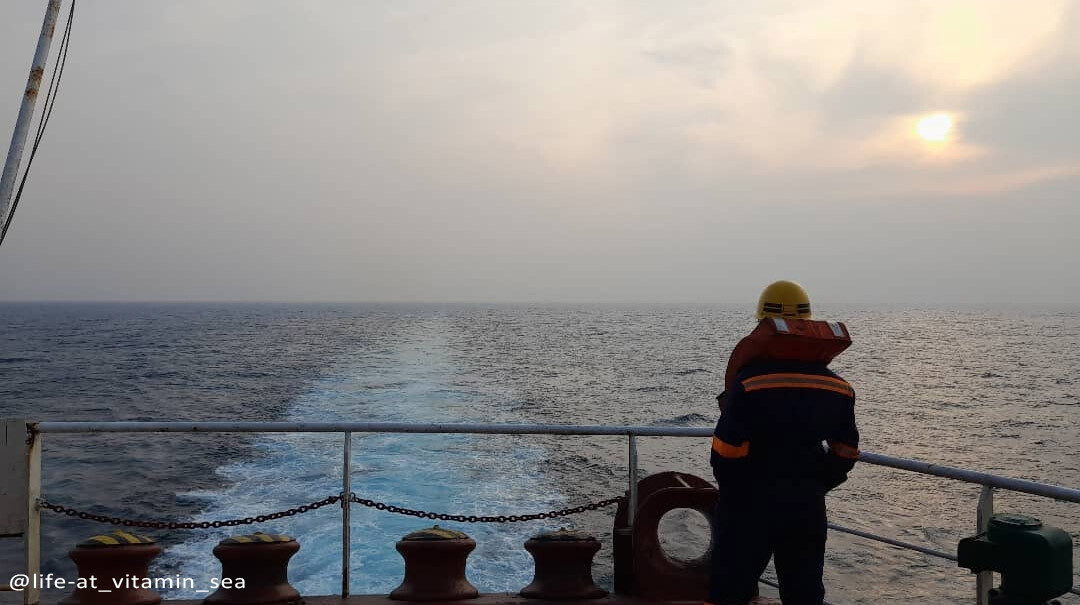 A ship's crew wearing yellow helmet and life jacket watching at the vast ocean behind the ship.
