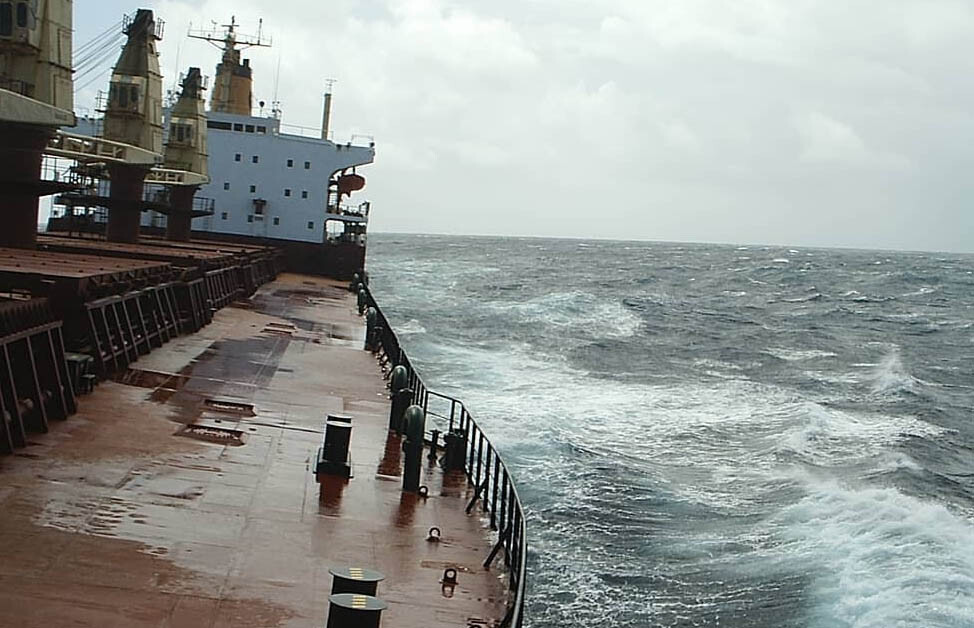 A general cargo vessel sailing across a slightly rough ocean as seen from the ship's port bow.