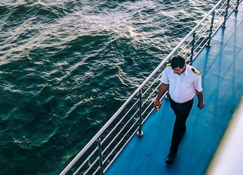 A ship officer walking on the ship's deck holding a radio.