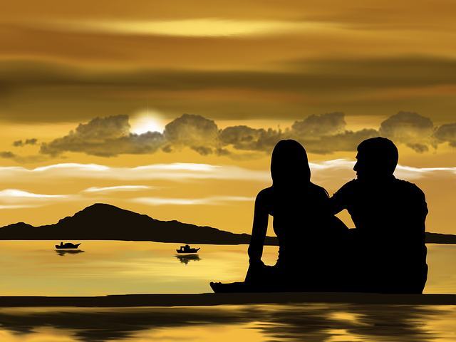 Two lovers sitting in the shore while watching a very beautiful sunset.