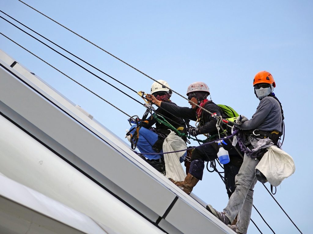 Seafarers working aloft greasing the crane wires of a general cargo vessel.