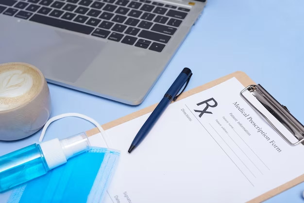 A prescription paper with pen beside a laptop.