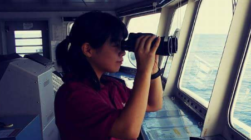 Holding a binocular with both hands while performing lookout duties on the bridge during navigation.