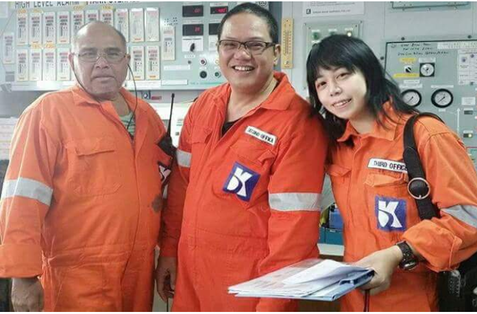 Hiroka Suzuki in orange coverall with two other male crewmates in a photo op while inside the cargo control room.
