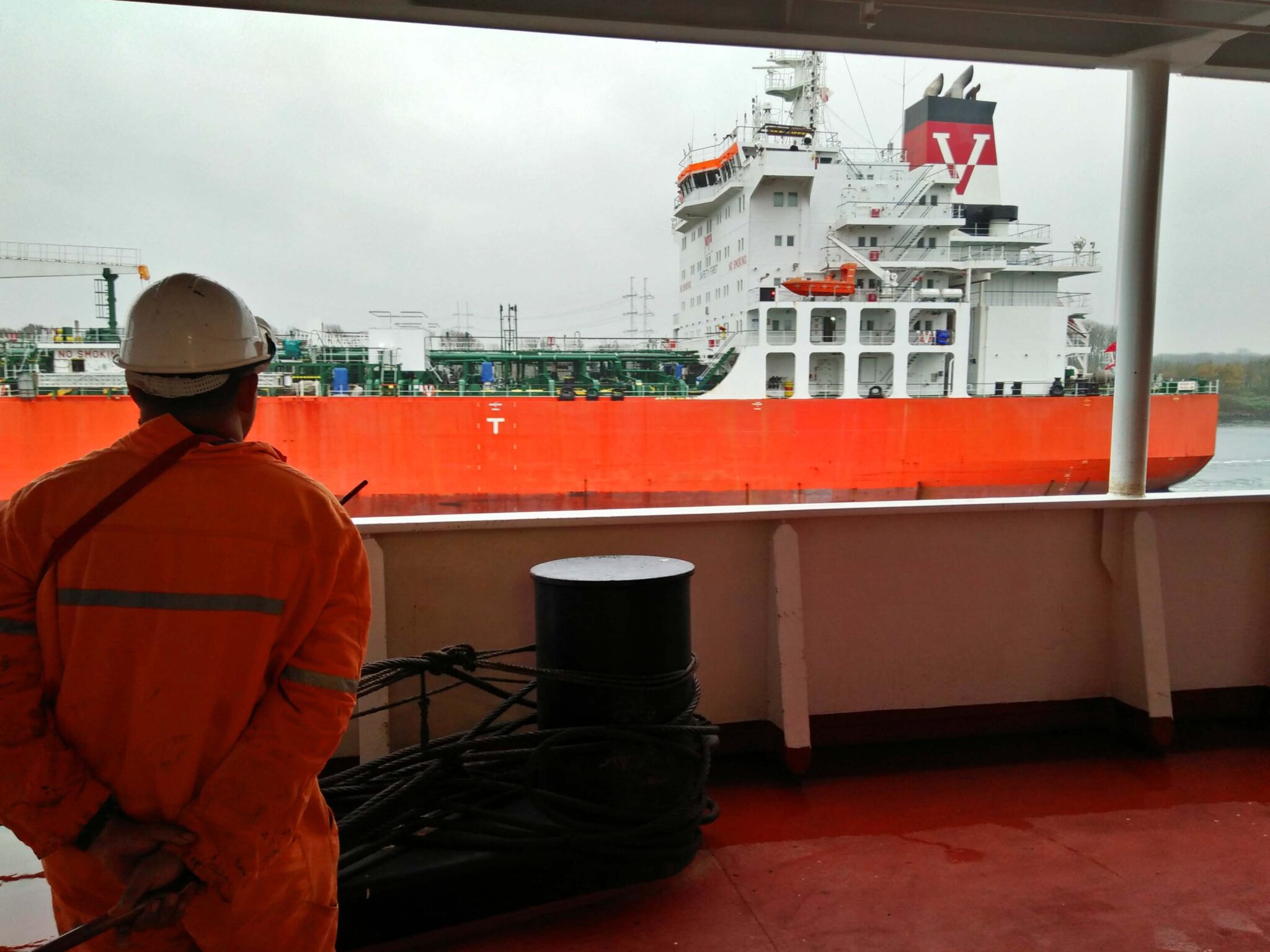 A seafarer in orange coverall on board watching another tanker vessel pass by.