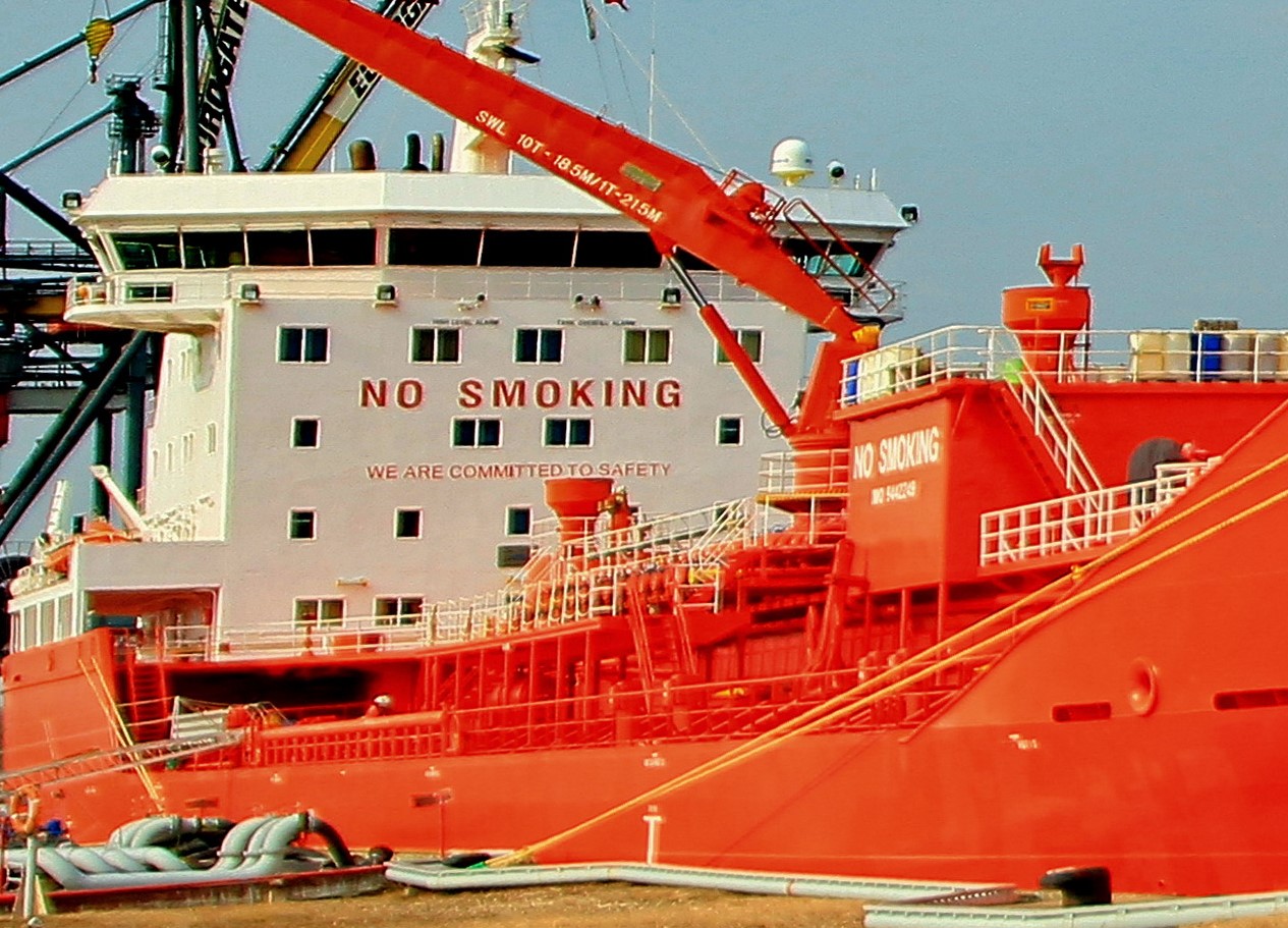 An orange tanker ship decked in port using starboard side alongside.