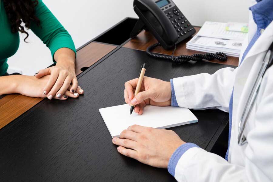 Doctor writing something on a piece of paper with a patient in front of him.