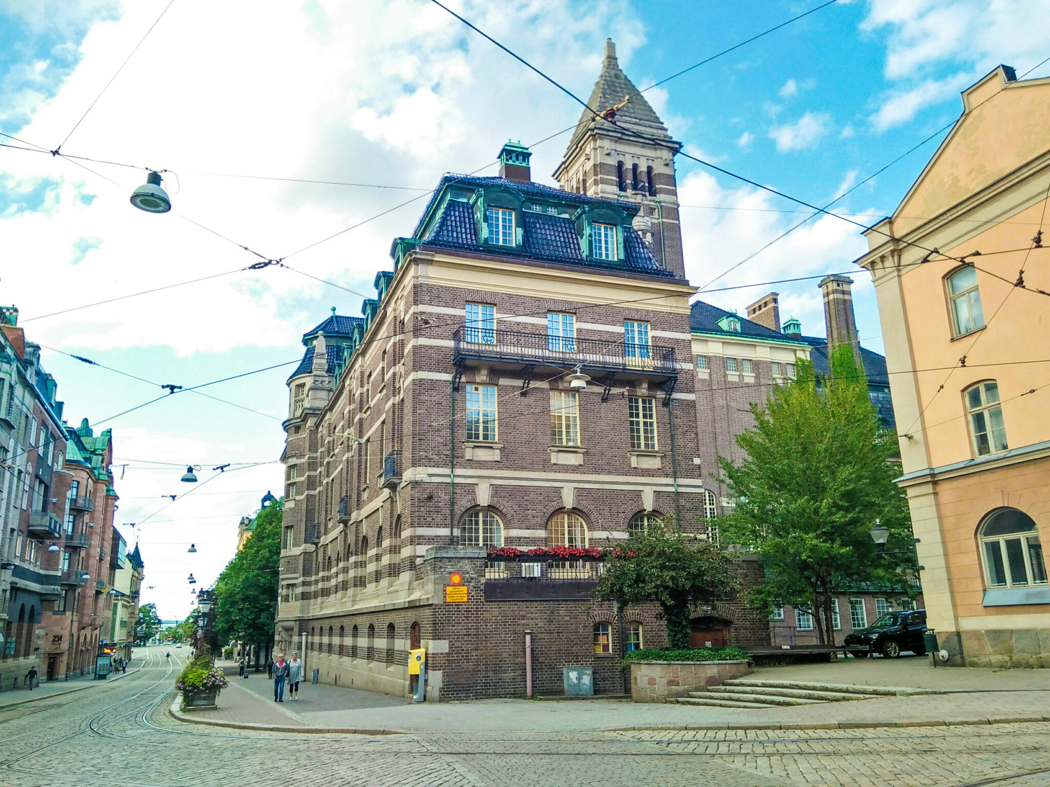 A street in Aalborg, Denmark with tram tracks, old-style brick buildings, and people walking in the sidewalks.