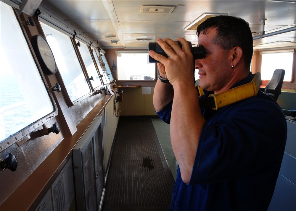 Seaman on the bridge using a binocular and looking out for target as part of his watch and lookout duties.