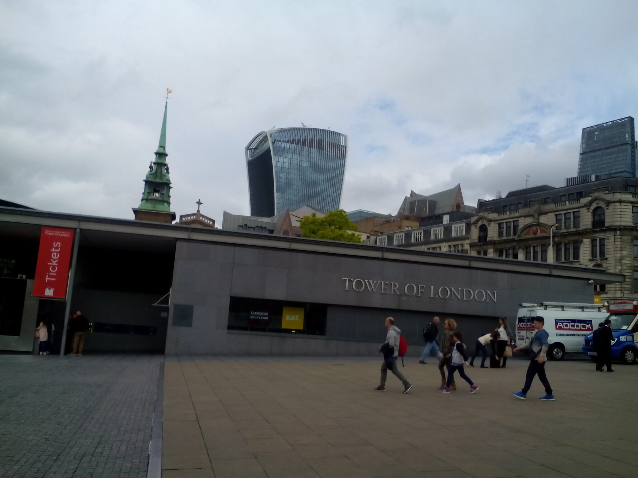 Tourist passing near the front of a ticket booth with a view of the weird-looking Walkie-Talkie Building.
