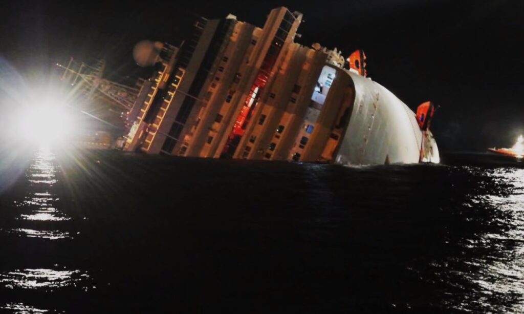 The cruise vessel Costa Concordia with her starboard side listed underwater during the night.