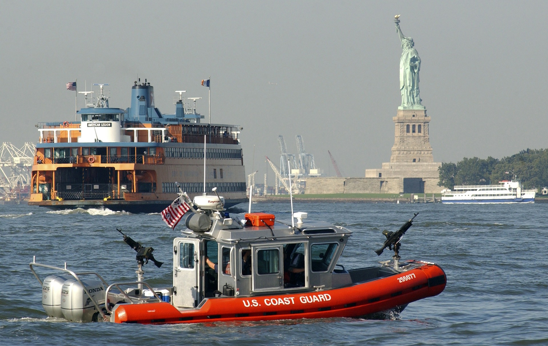 Statue of Liberty in New York Bay with ferries crossing and a US Coast Guard on Stand By.