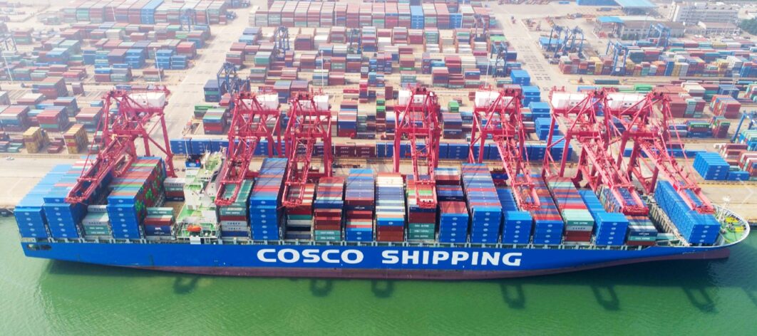 A blue COSCO container ship docked in port.