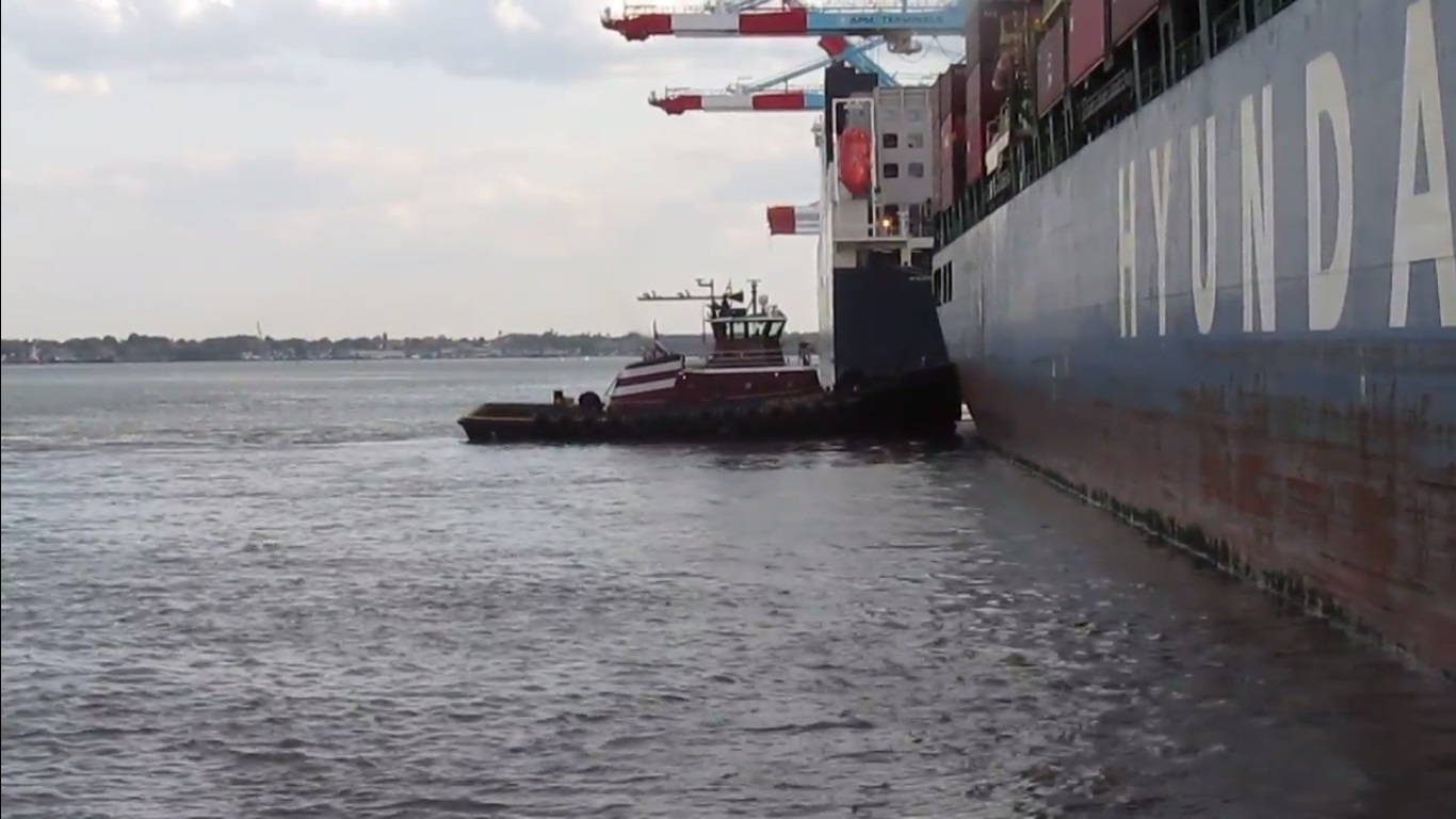 A tractor tugboat pushing a vessel to get it alongside
