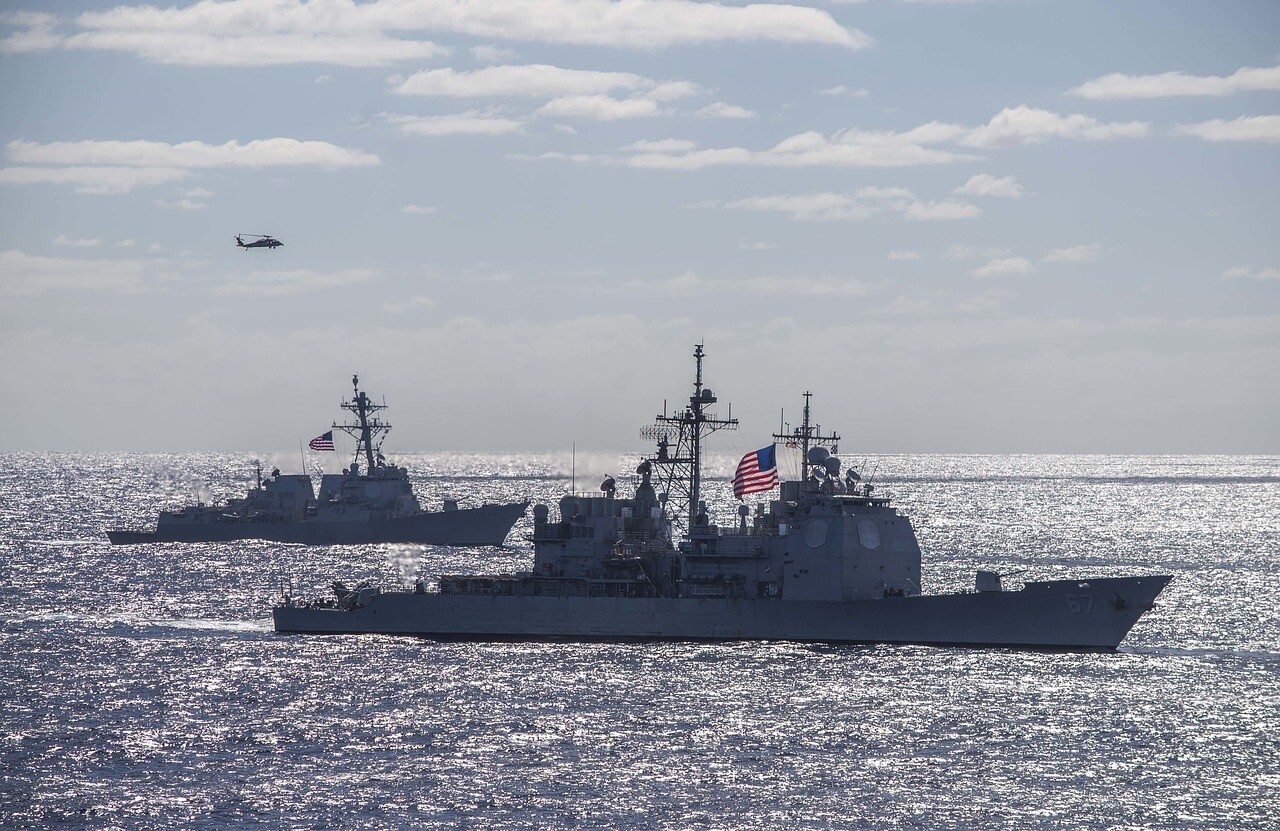 USS Cole Destroyer raising the American flag while sailing with other warships.