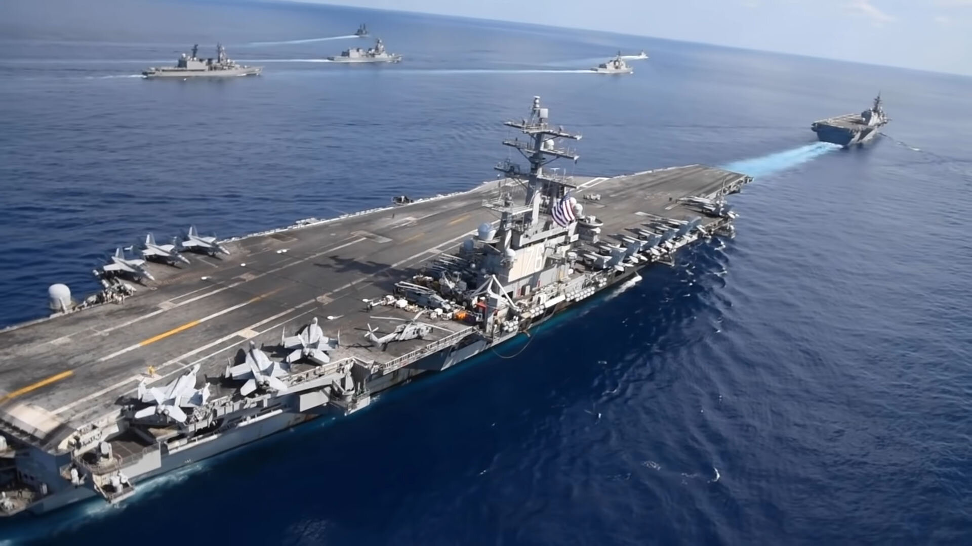 Two aircraft carriers with helicopters and aircrafts on its deck. She is surrounded by destroyers and Frigates.