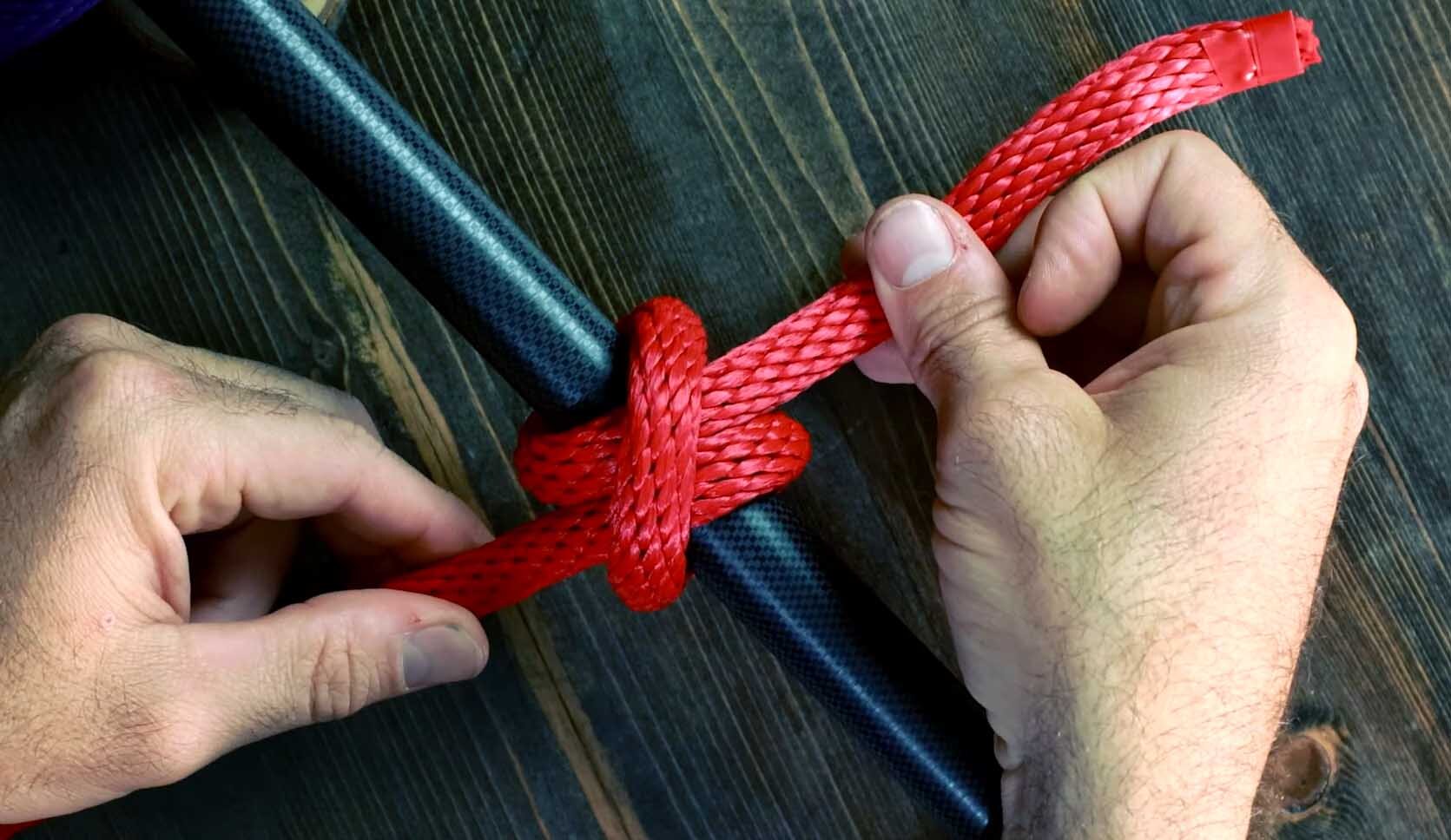 Tying a Clove Hitch Rope End Method using a red rope on a black pole.