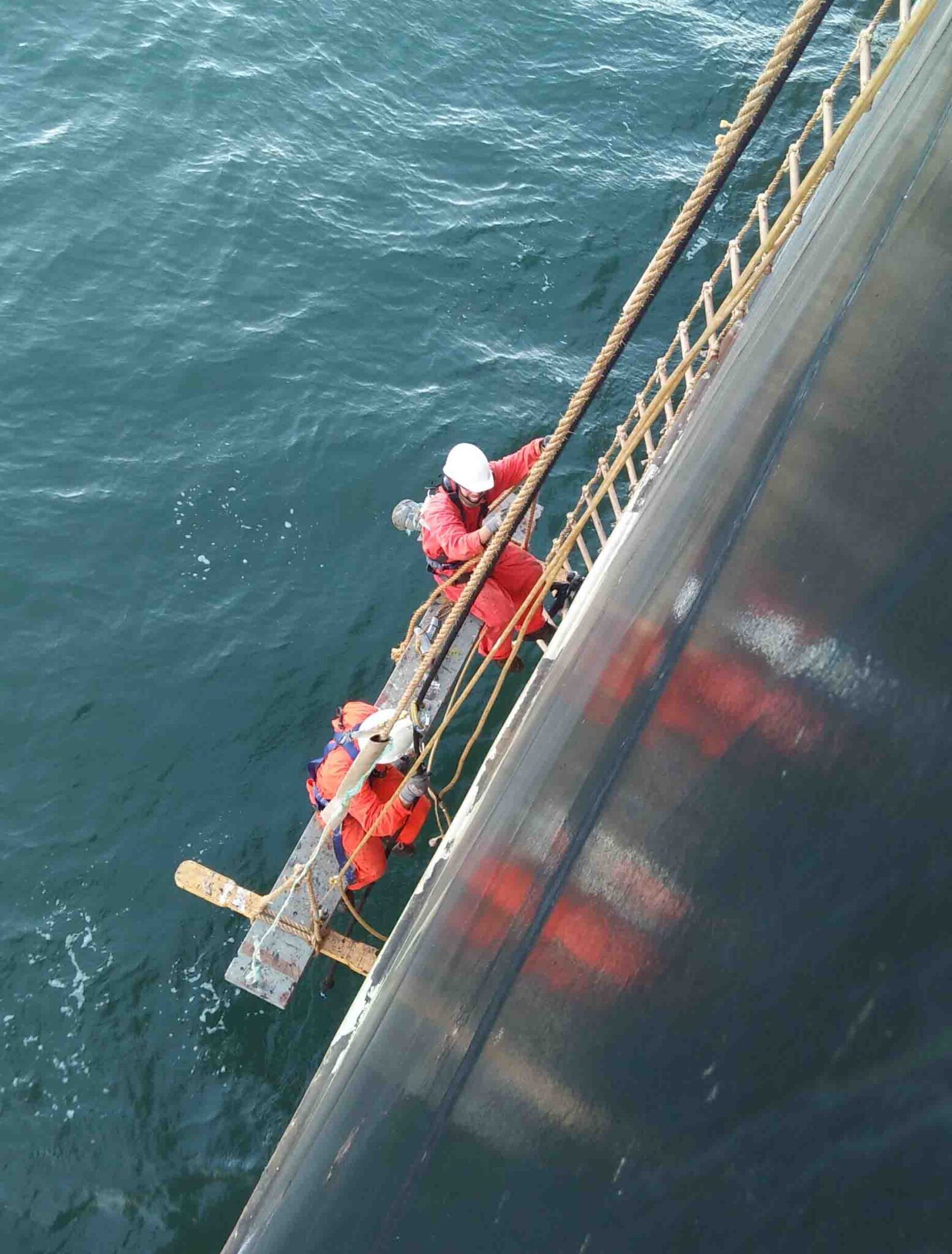 Deck crew using a Stage Plank, Gondola, or Gindola while working over the ship's side.