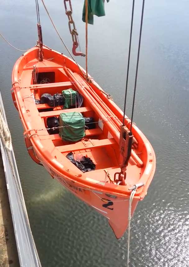 An orange Open -Type Lifeboat hanging by the ship's side using a davit.