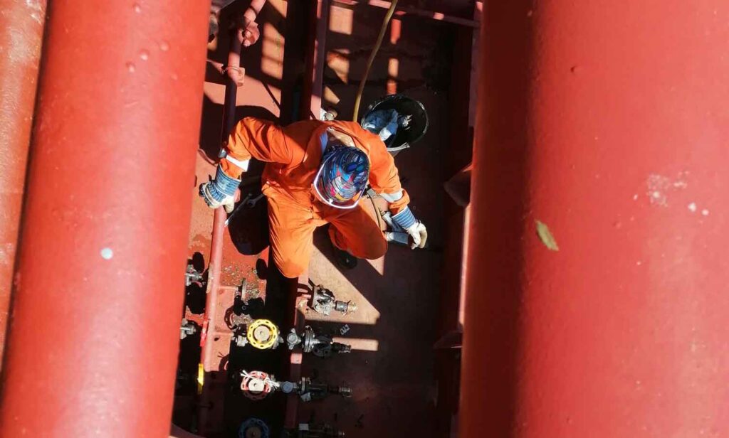 A deck crew wearing PPE chipping on the deck of a tanker vessel.