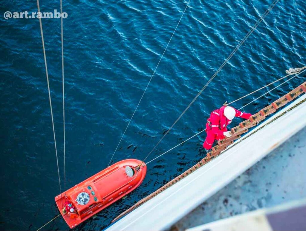 A crew climbing down the embarkation ladder while the lifeboat below her waits on the water.