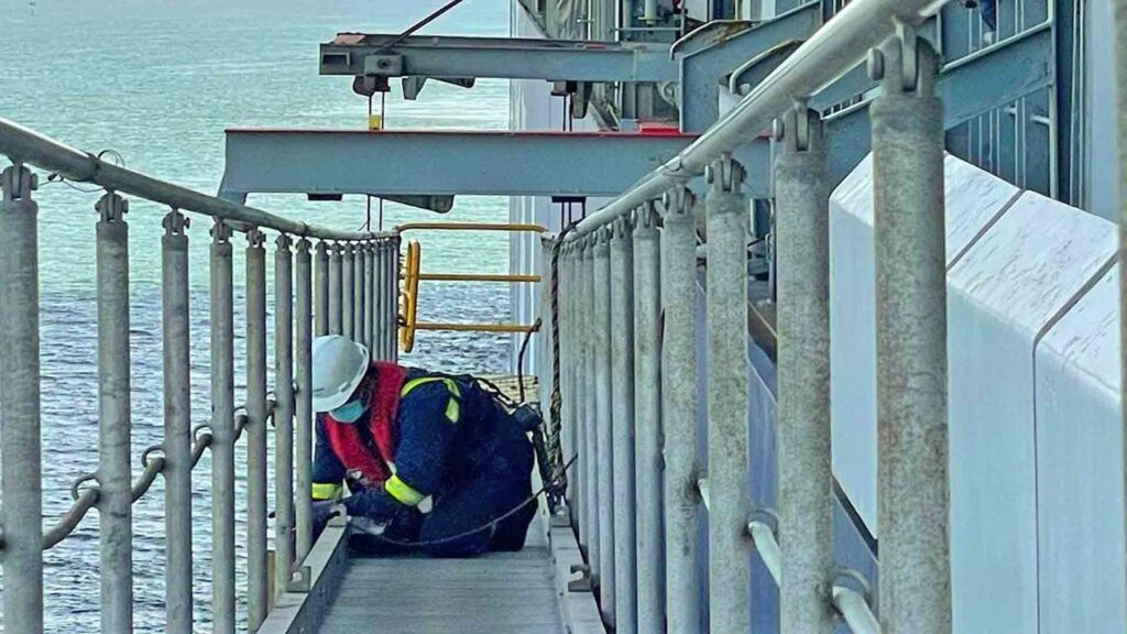 A crew equipped with safety harnesses and lifejackets securing the seaside accommodation ladder.