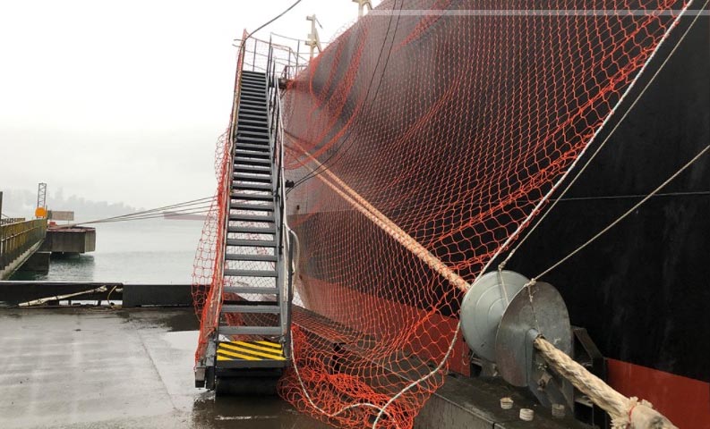 An accommodation ladder rigged on the jetty with mooring lines passing below it. There is also a safety net and operating wires that are slacked.