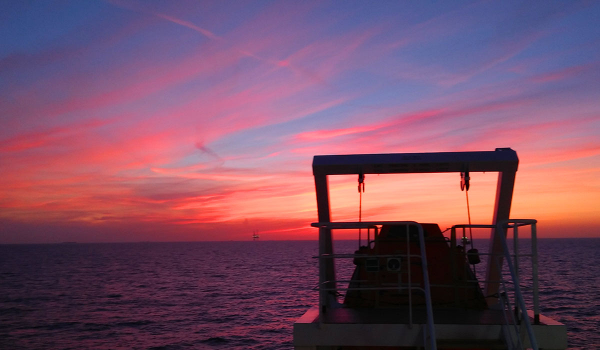 Beautiful sunrise with shades of red and orange on the horizon as viewed near the ship's lifeboat.