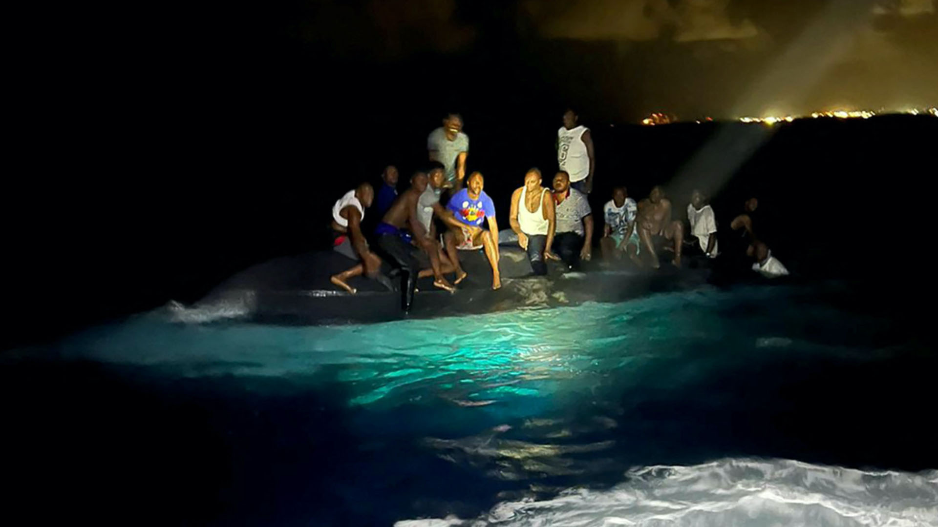 Survivors sitting on the hull of the capsized boat during nighttime.