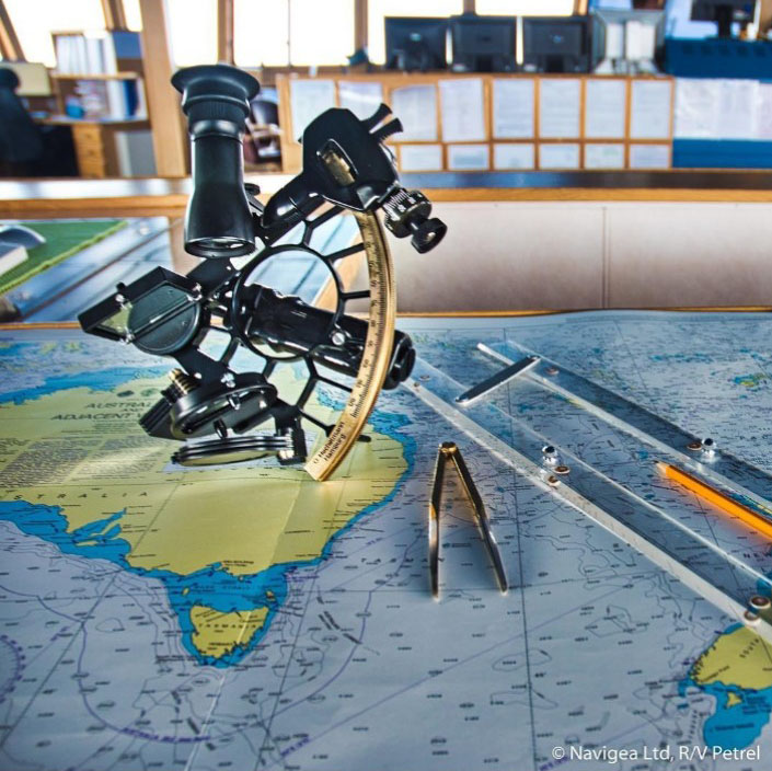 A marine sextant beside a compass divider and parallel rulers on top of a nautical chart.
