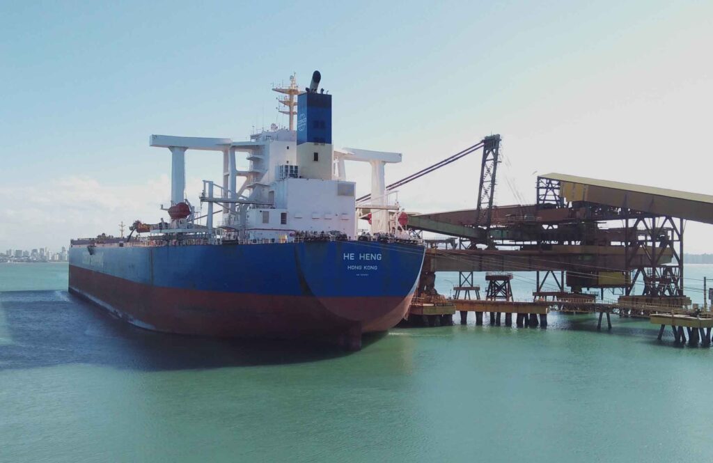 A blue bulk carrier loading her cargo in a Brazilian port during a sunny day.