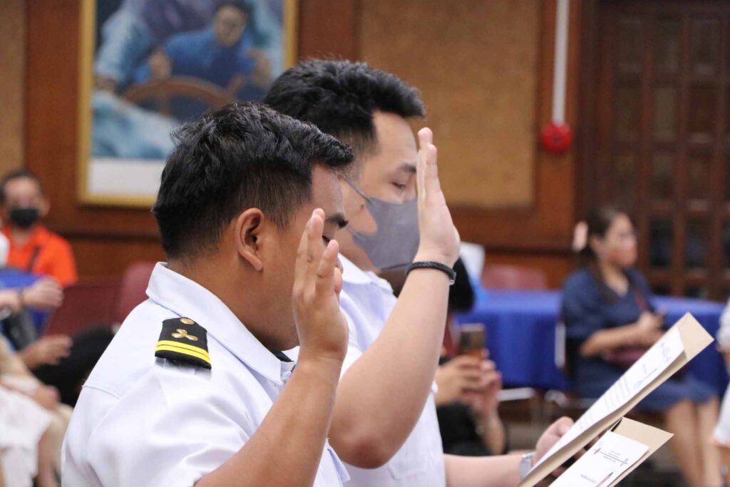 Two licensure passers raising their right hand during the oath taking ceremony.