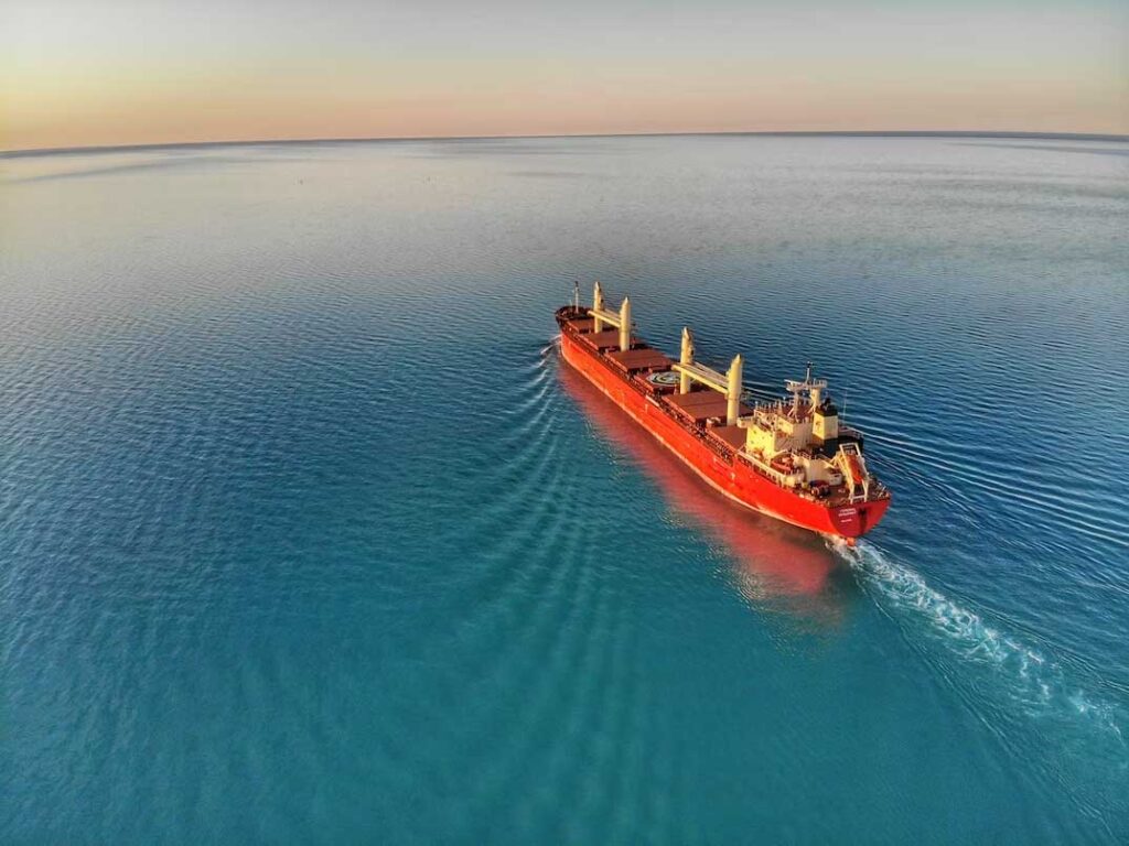 A red cargo ship navigating in the calm blue ocean during sunset.