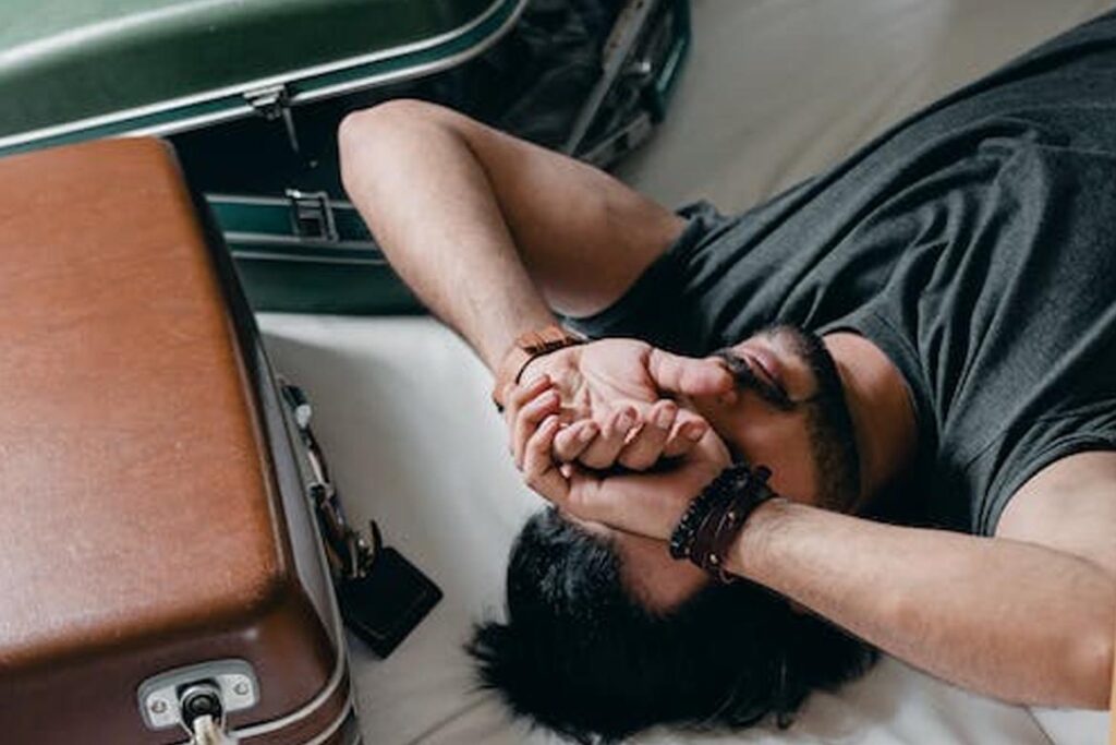 A man and his two luggage lying in bed. He looks stressed and this may also be a topic for your cruise ship interview questions.