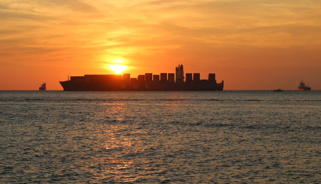 A container ship sailing on the high seas with a golden sunset behind her.