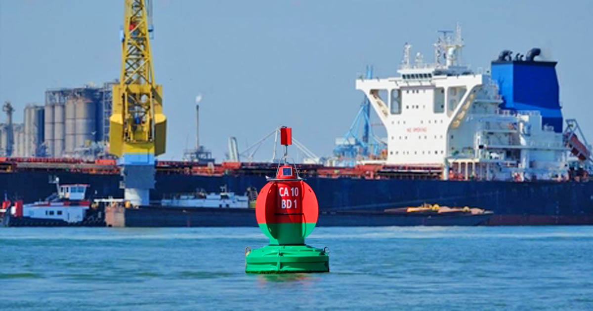 A buoy with red over green color placed in port with a view of a huge ship far behind it docked in the jetty.