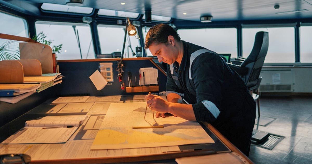 An Officer of the Watch (OOW) inside the chart room plotting his position in the nautical charts,