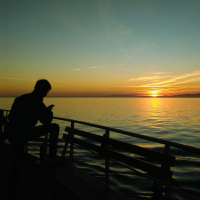 A seaman using his mobile phone while watching a beautiful sunset on on calm waters.