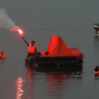 A trainee holding a hand flare while on top of a liferaft during their basic safety training.