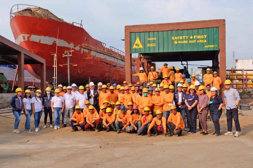 The whole crew and staffs of Western Shipyard Services, Inc. in a photo op with a vessel on the background.