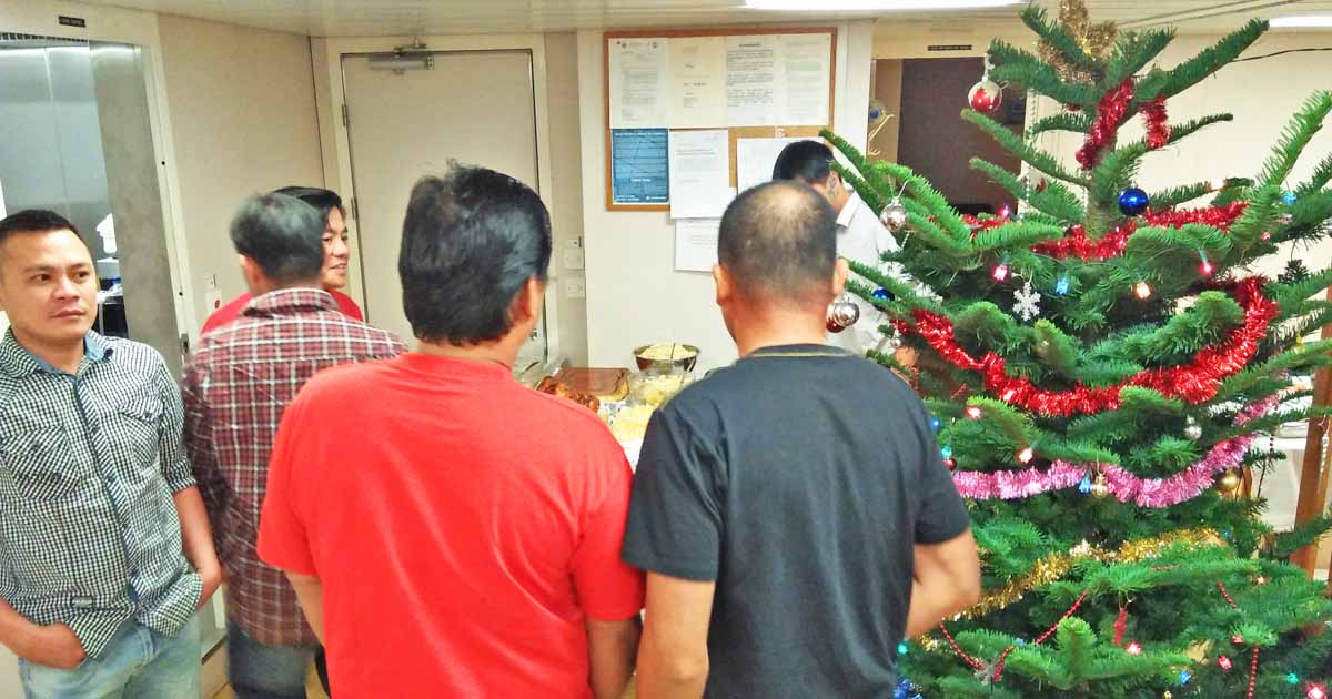 Seafarers standing in the mess hall beside a tall Christmas tree preparing for dinner.
