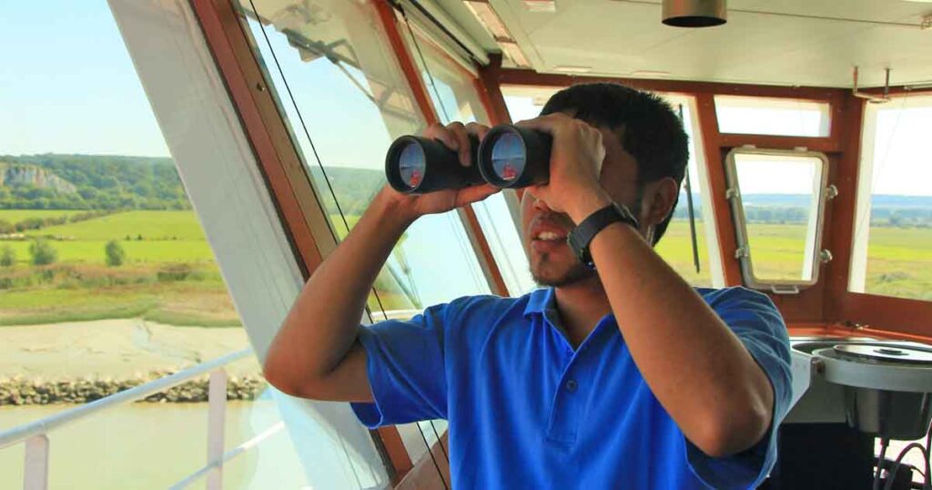 A ship's lookout using a binocular to take a good look at the target ship.