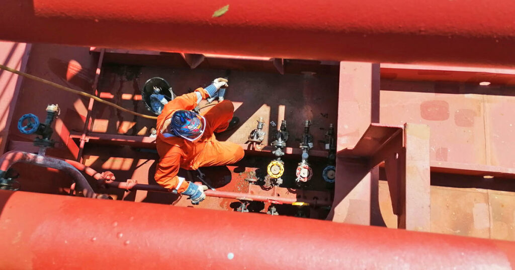 A crew working under the pipeline of a tanker vessel.