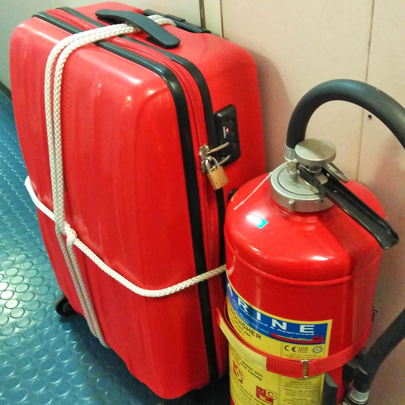 A red luggage placed beside a red fire extinguisher.