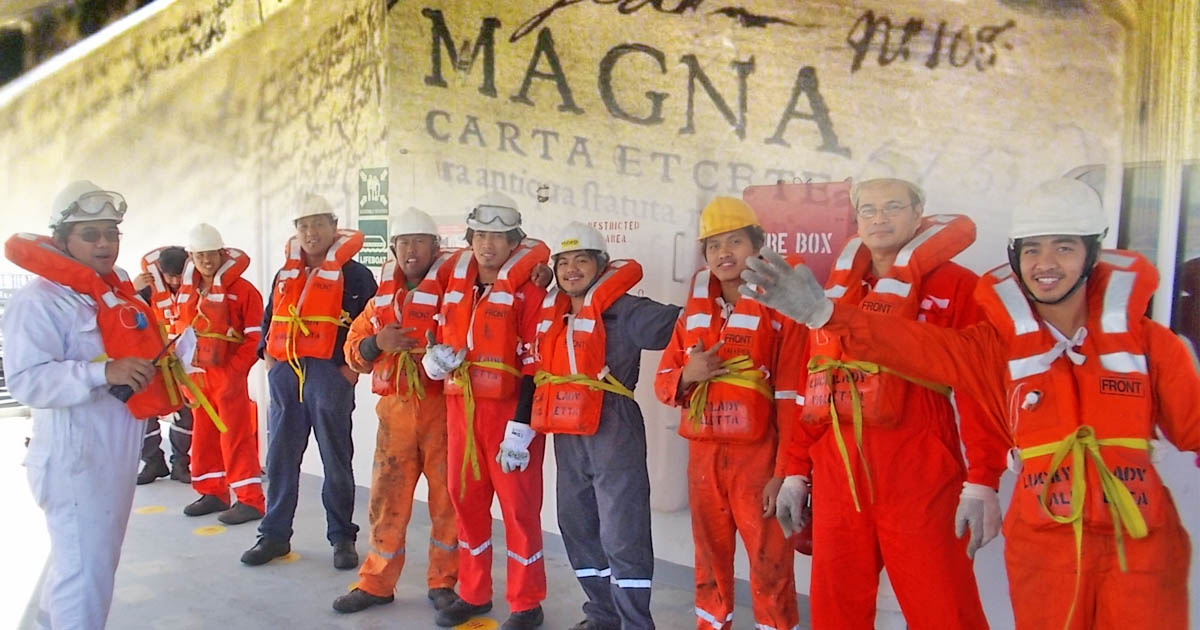 Filipino seafarers standing on deck wearing coveralls and lifejackets.
