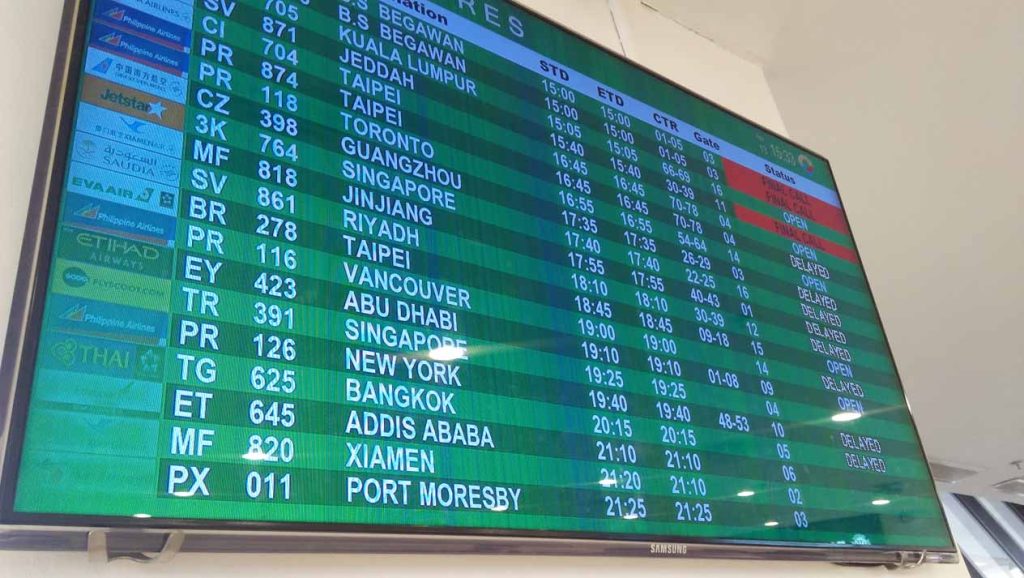 Flight schedule monitor showing the destinations, flight numbers, departure times, and status.