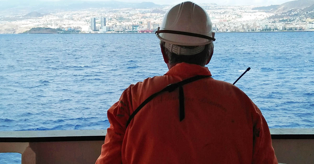 A seafarer standing on the ship's deck looking out to the distant city.